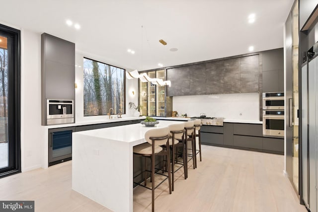 kitchen with beverage cooler, modern cabinets, a kitchen island, light countertops, and a kitchen bar