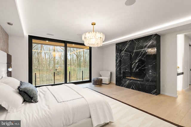 bedroom with expansive windows, a chandelier, wood finished floors, and a premium fireplace