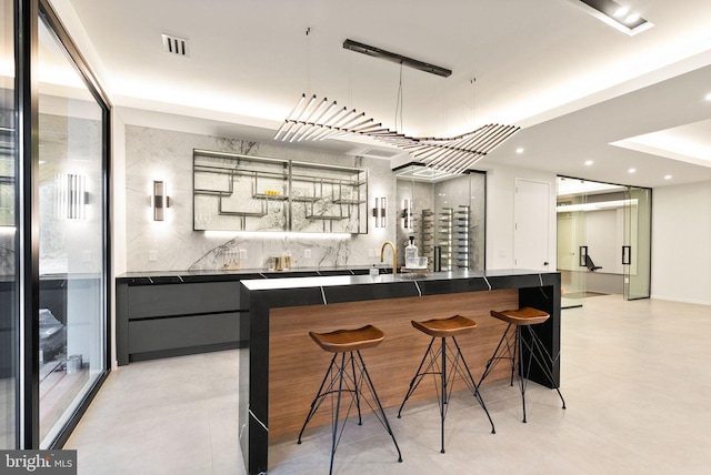 kitchen with tasteful backsplash, dark countertops, visible vents, and a kitchen bar