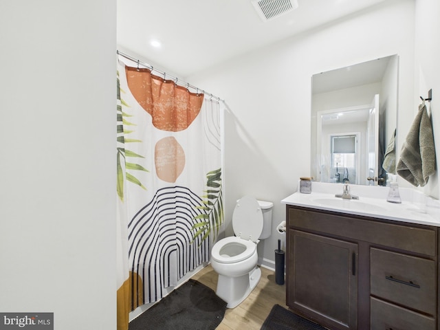 bathroom with toilet, a shower with shower curtain, wood finished floors, vanity, and visible vents