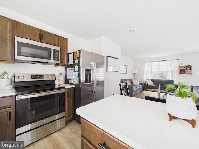 kitchen featuring light wood finished floors, stainless steel appliances, light countertops, and open floor plan