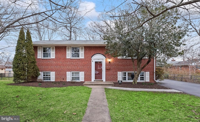 raised ranch featuring brick siding, a front lawn, and fence