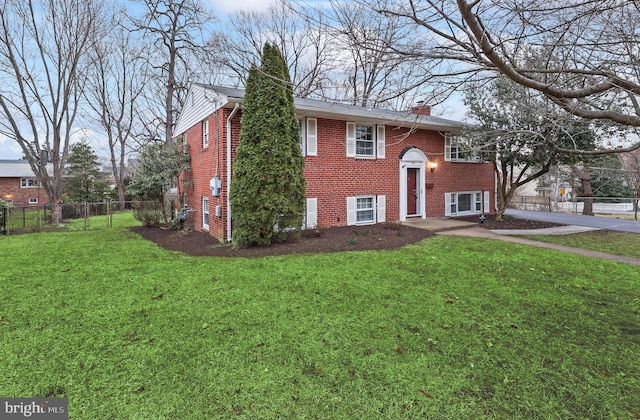 bi-level home featuring brick siding, a chimney, a front yard, and fence