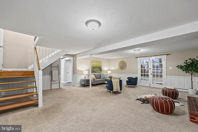 carpeted living room featuring french doors, a textured ceiling, wainscoting, and stairs