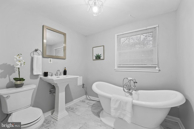 bathroom with marble finish floor, a freestanding bath, toilet, and baseboards