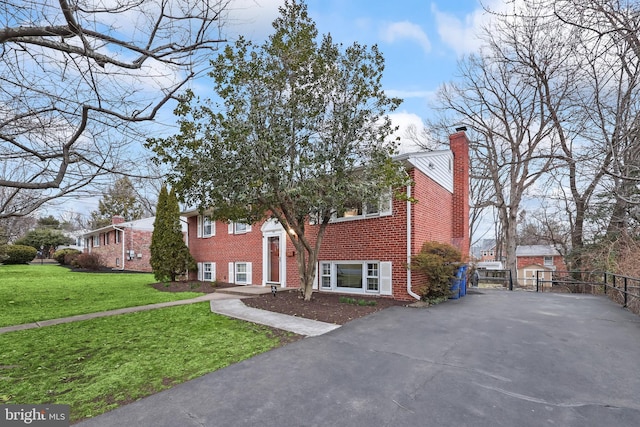 raised ranch with brick siding, fence, a front yard, a chimney, and driveway