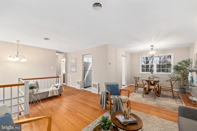 living room with visible vents, baseboards, an inviting chandelier, and wood finished floors