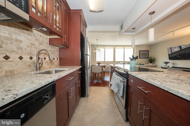 kitchen with light tile patterned floors, decorative backsplash, appliances with stainless steel finishes, a sink, and light stone countertops