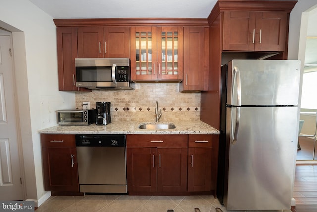 kitchen featuring a toaster, tasteful backsplash, appliances with stainless steel finishes, light stone countertops, and a sink