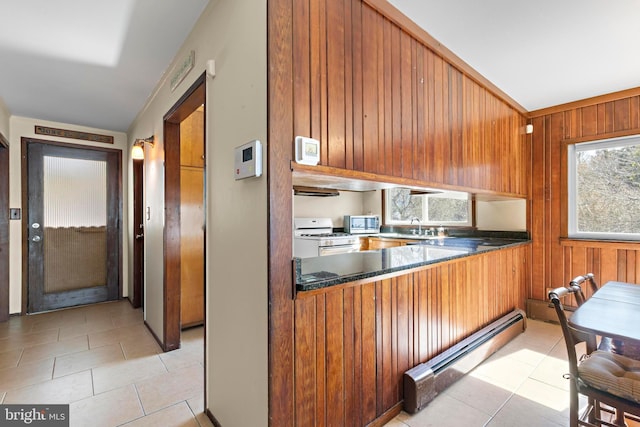 kitchen with brown cabinets, stainless steel microwave, a baseboard heating unit, wood walls, and white gas range