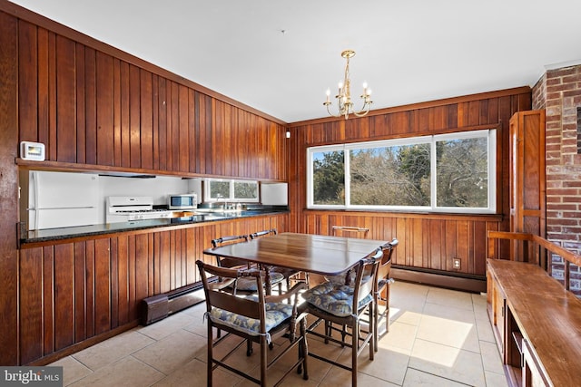 dining room featuring a baseboard heating unit, light tile patterned floors, a notable chandelier, and wood walls