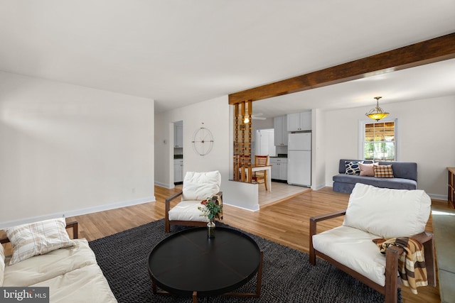 living room featuring beam ceiling, light wood-style floors, and baseboards