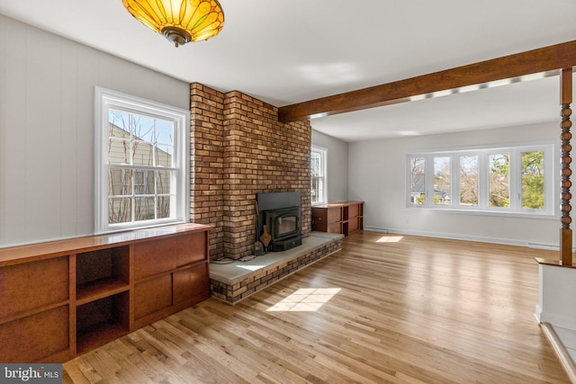 unfurnished living room featuring beam ceiling, light wood-style flooring, baseboards, and a wood stove