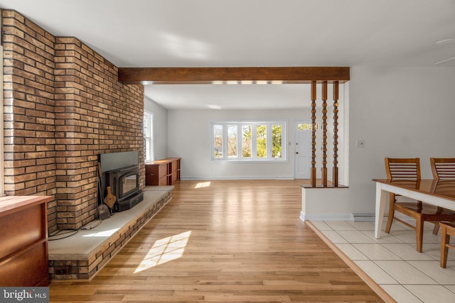 living area featuring baseboards, beam ceiling, a wood stove, and light wood finished floors