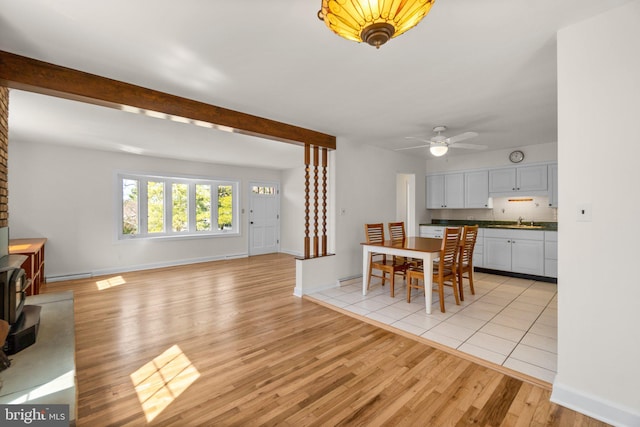 dining room with light wood-type flooring, beam ceiling, baseboards, and a wood stove