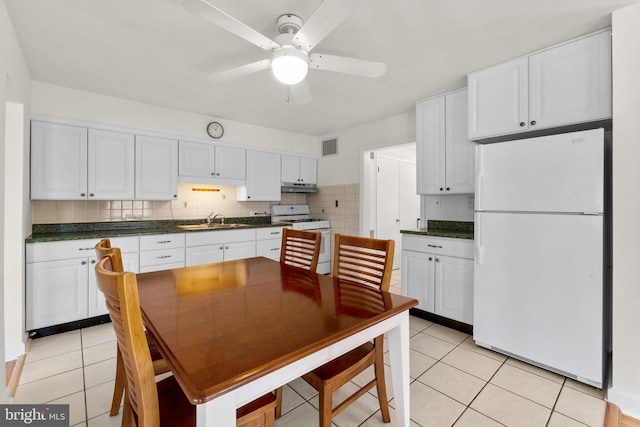 kitchen with dark countertops, under cabinet range hood, light tile patterned floors, white appliances, and a sink