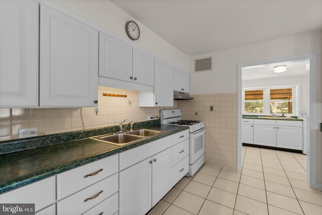 kitchen featuring dark countertops, white gas stove, under cabinet range hood, white cabinetry, and a sink