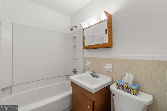 bathroom with a wainscoted wall, toilet, vanity, shower / bath combination, and tile walls