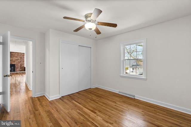 unfurnished bedroom featuring hardwood / wood-style flooring, a closet, a baseboard radiator, baseboards, and a brick fireplace