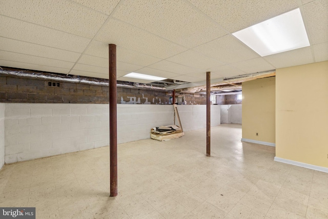 finished below grade area featuring tile patterned floors, concrete block wall, a paneled ceiling, and baseboards