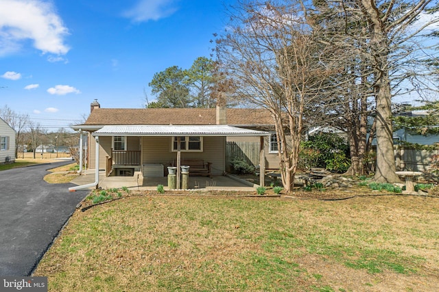 rear view of property with aphalt driveway, a lawn, a porch, and a chimney