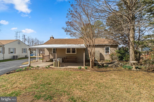 back of house featuring driveway, a yard, central AC, a chimney, and a carport