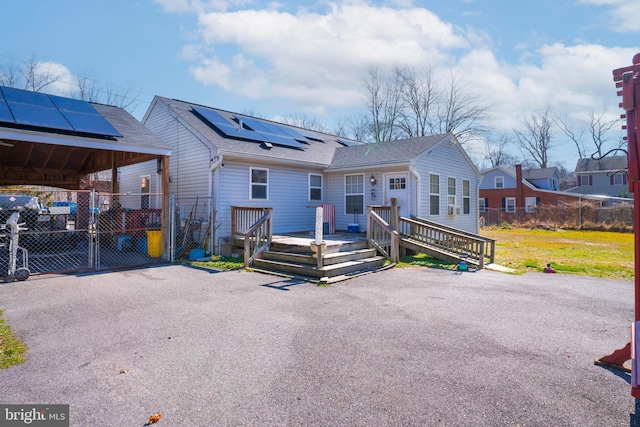 view of front facade featuring a deck, a gate, roof mounted solar panels, fence, and a shingled roof