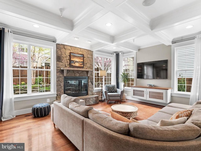 living room featuring beamed ceiling, coffered ceiling, wood finished floors, and a stone fireplace