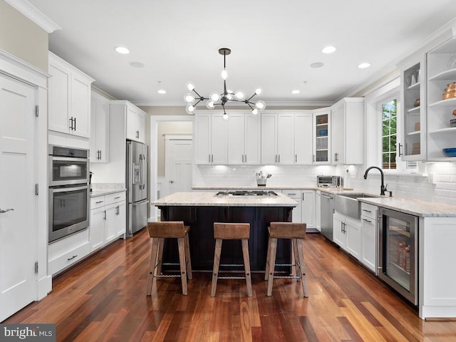 kitchen with beverage cooler, a sink, white cabinets, appliances with stainless steel finishes, and a center island