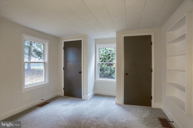 unfurnished room with carpet floors, baseboards, visible vents, and built in features