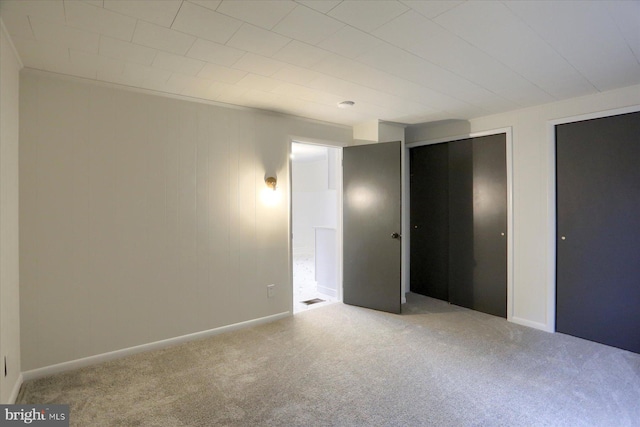 unfurnished bedroom featuring carpet, two closets, and baseboards