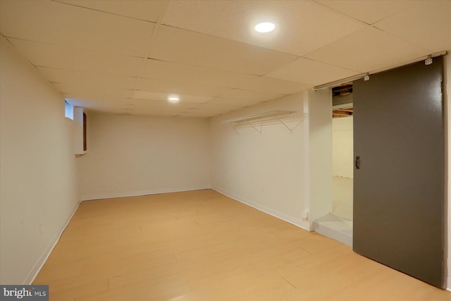 finished below grade area featuring light wood-type flooring, a paneled ceiling, and baseboards