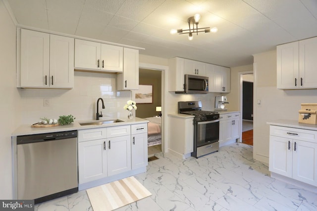 kitchen featuring white cabinets, marble finish floor, stainless steel appliances, and a sink