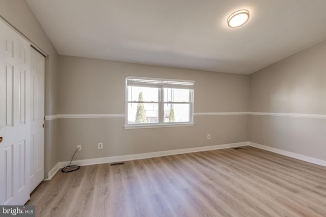 spare room featuring wood finished floors, visible vents, and baseboards