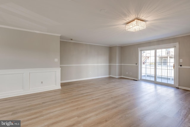 empty room with crown molding, light wood finished floors, and wainscoting