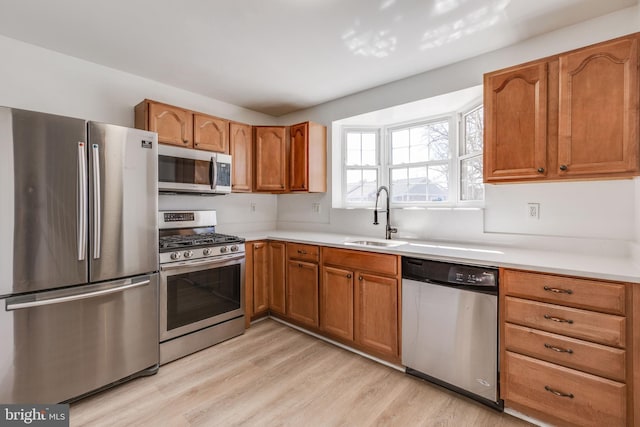 kitchen featuring light wood-type flooring, stainless steel appliances, light countertops, and a sink