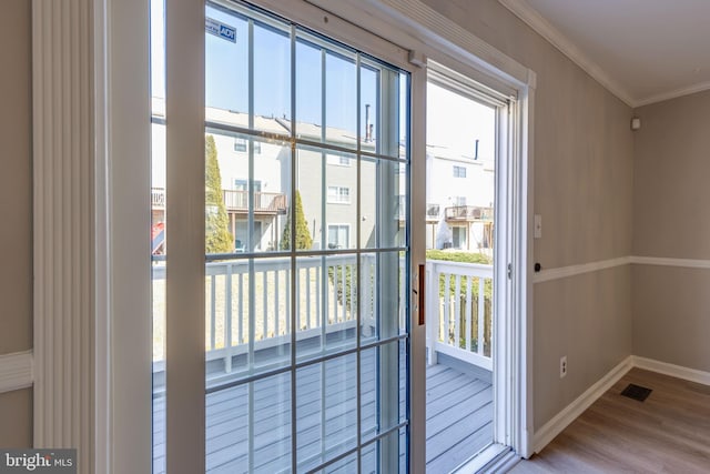 doorway featuring wood finished floors, a healthy amount of sunlight, baseboards, and ornamental molding