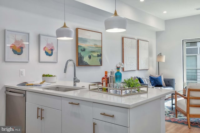 kitchen with light countertops, a sink, light wood-style flooring, and stainless steel dishwasher