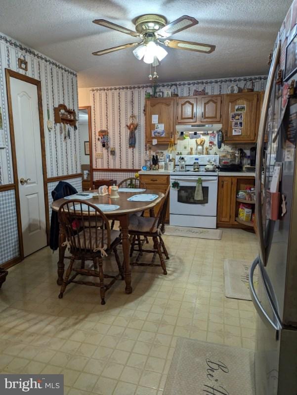 kitchen featuring under cabinet range hood, freestanding refrigerator, light floors, white range with electric cooktop, and wallpapered walls