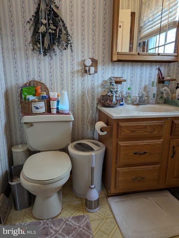 half bath featuring toilet, wallpapered walls, visible vents, and vanity