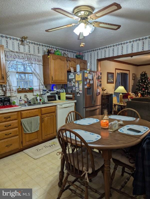 kitchen featuring a textured ceiling, white dishwasher, stainless steel refrigerator with ice dispenser, light floors, and wallpapered walls