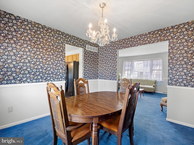 carpeted dining room with a chandelier, visible vents, baseboards, wainscoting, and wallpapered walls