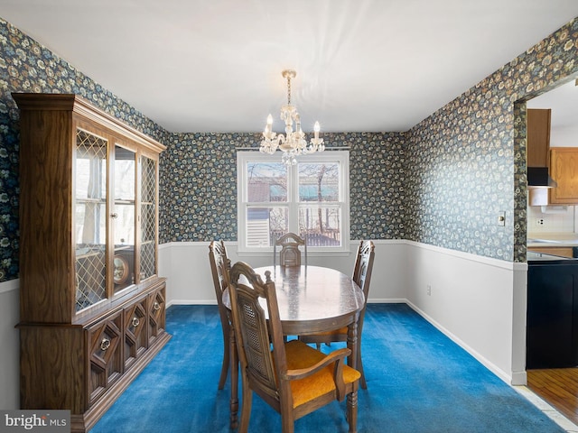 carpeted dining room featuring a wainscoted wall, a notable chandelier, baseboards, and wallpapered walls