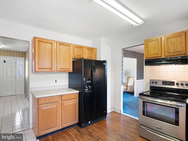 kitchen with under cabinet range hood, electric range, light countertops, dark wood-style floors, and black refrigerator with ice dispenser