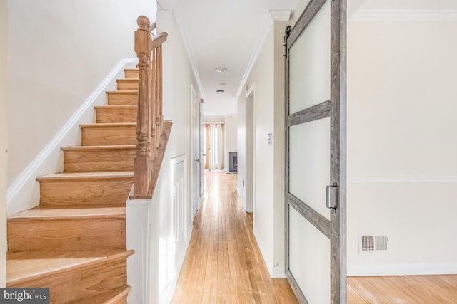 staircase featuring wood finished floors, visible vents, crown molding, and a barn door