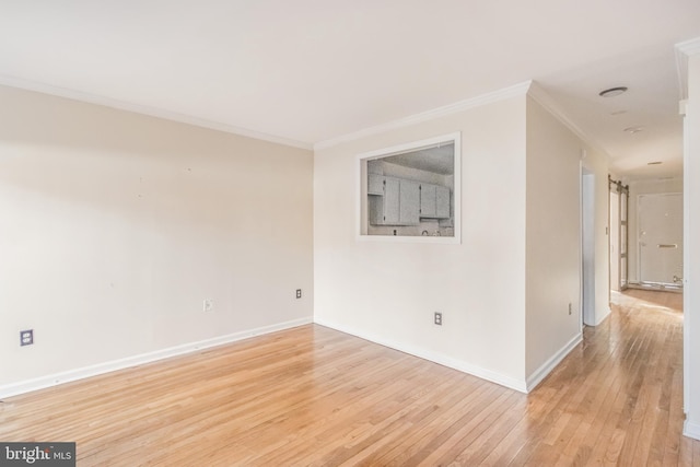 empty room with light wood-style floors, ornamental molding, baseboards, and a barn door