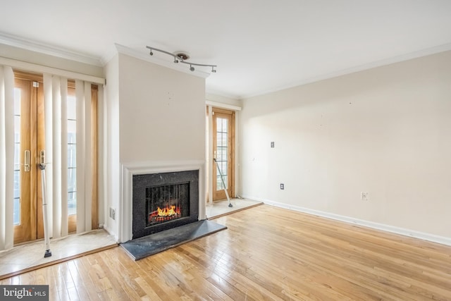 unfurnished living room featuring light wood-type flooring, baseboards, a warm lit fireplace, and crown molding