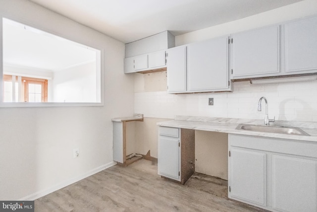 kitchen with a sink, baseboards, light countertops, backsplash, and light wood finished floors