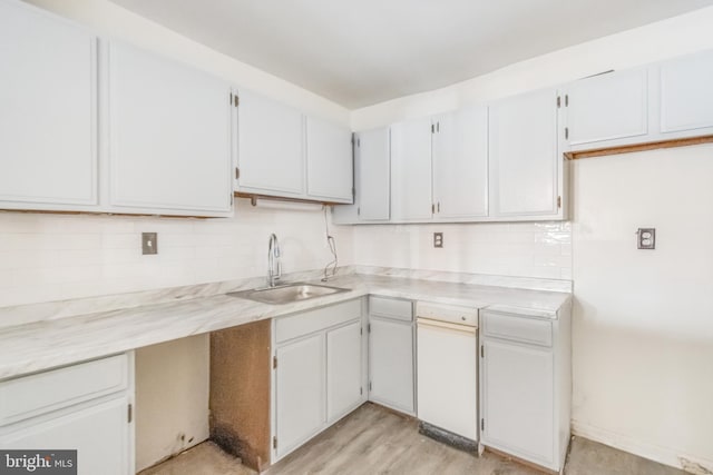 kitchen with a sink, light countertops, light wood-style floors, white cabinetry, and backsplash