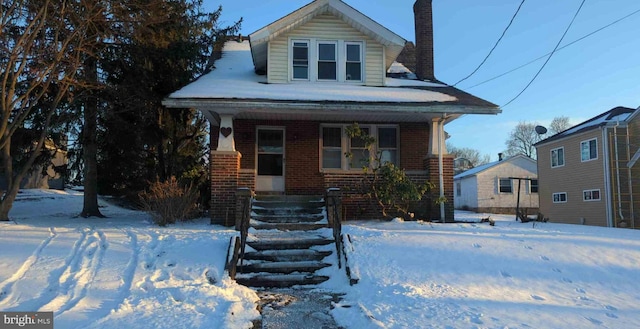 view of front of home with covered porch, brick siding, and a chimney